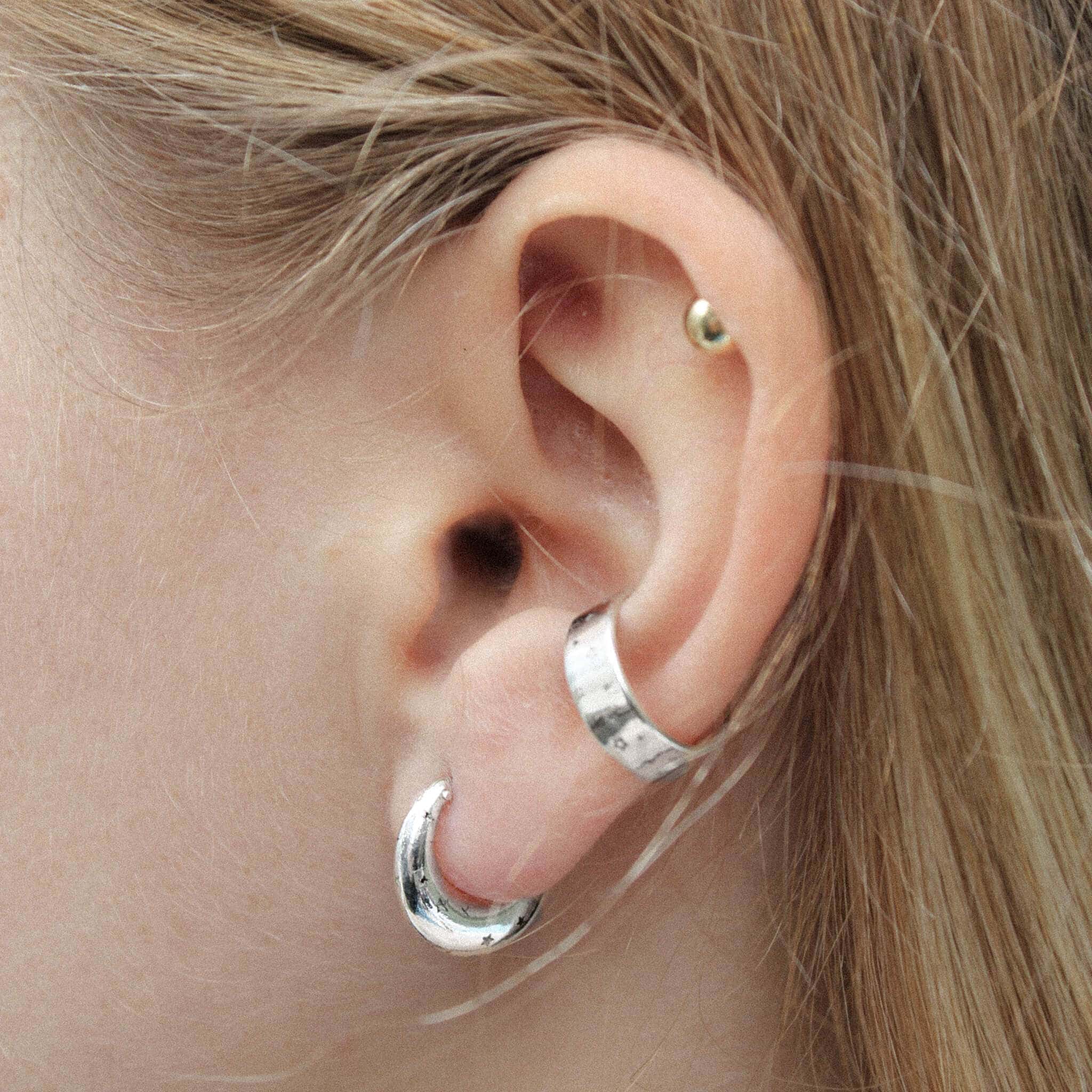 Silver star earrings and silver ear cuff on a model ear.