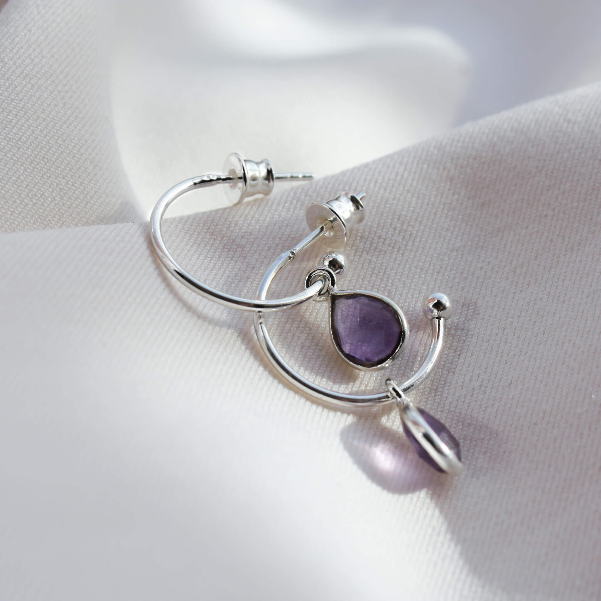 Silver hoop pendant earrings with amethyst on material.