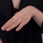 Modelka prezentuje na dłoni złoty pierścionek zaręczynowy z morganitem i diamentami. Obrana jest na czarno.