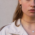 Modelka prezentuje na sobie choker z pereł i naszyjniik z grawerem BODY.