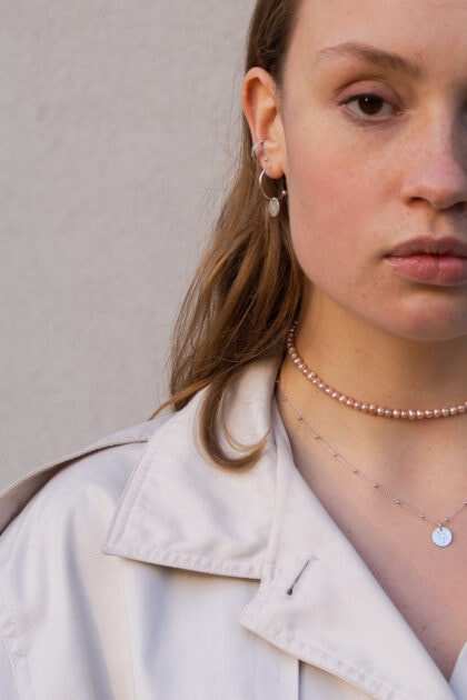 Modelka prezentuje na sobie choker z pereł i naszyjniik z grawerem BODY.