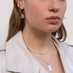 Modelka prezentuje na sobie srebrny naszyjnik z grawerem, żółty naszyjnik z cytrynem i kolczyki koła z zawieszką.