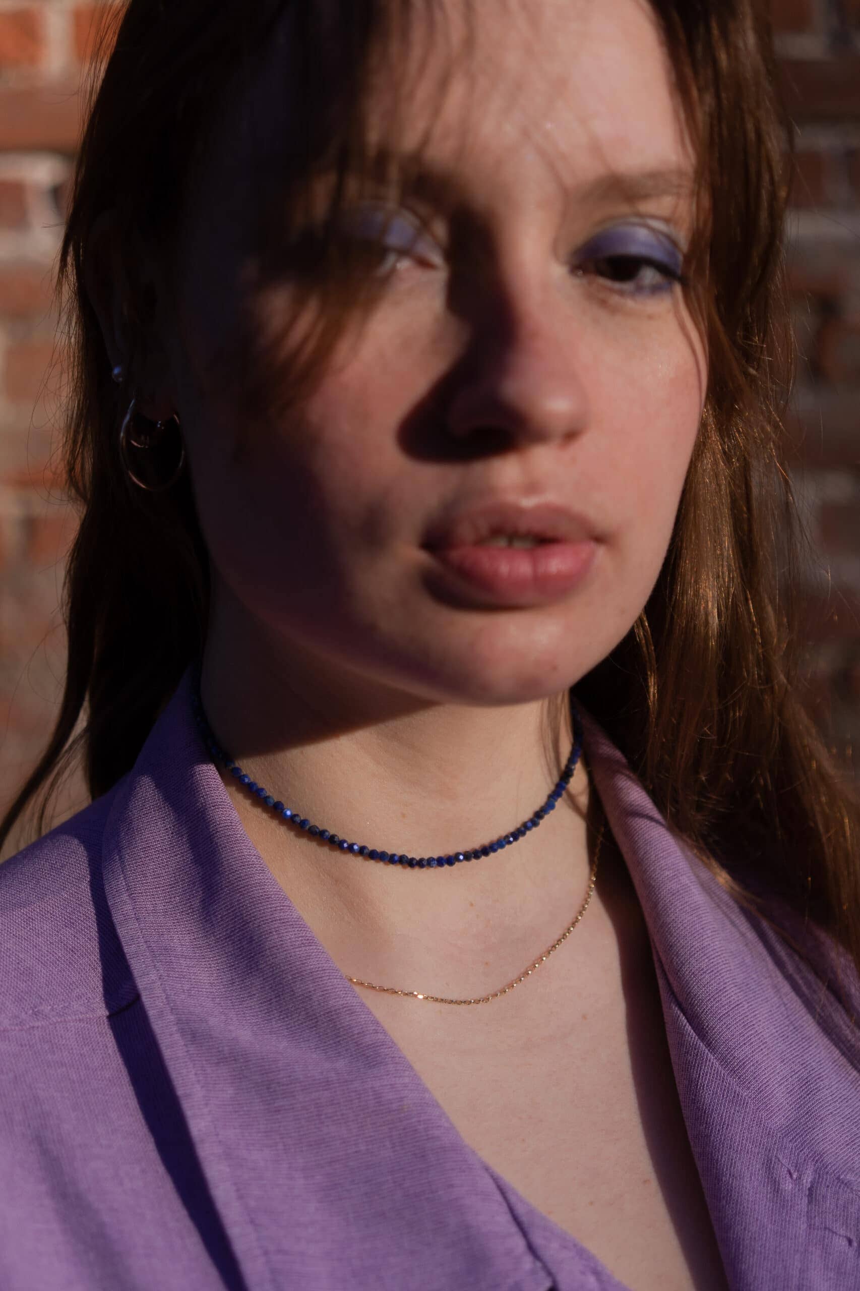 Modelka prezentuje naszyjnik z lapis lazuli i złotą biżuterię.
