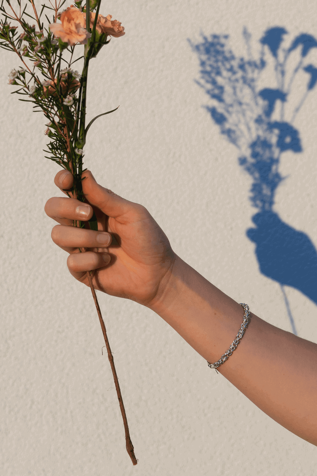 The model presents a silver bracelet on her hand, holding flowers in her hand.