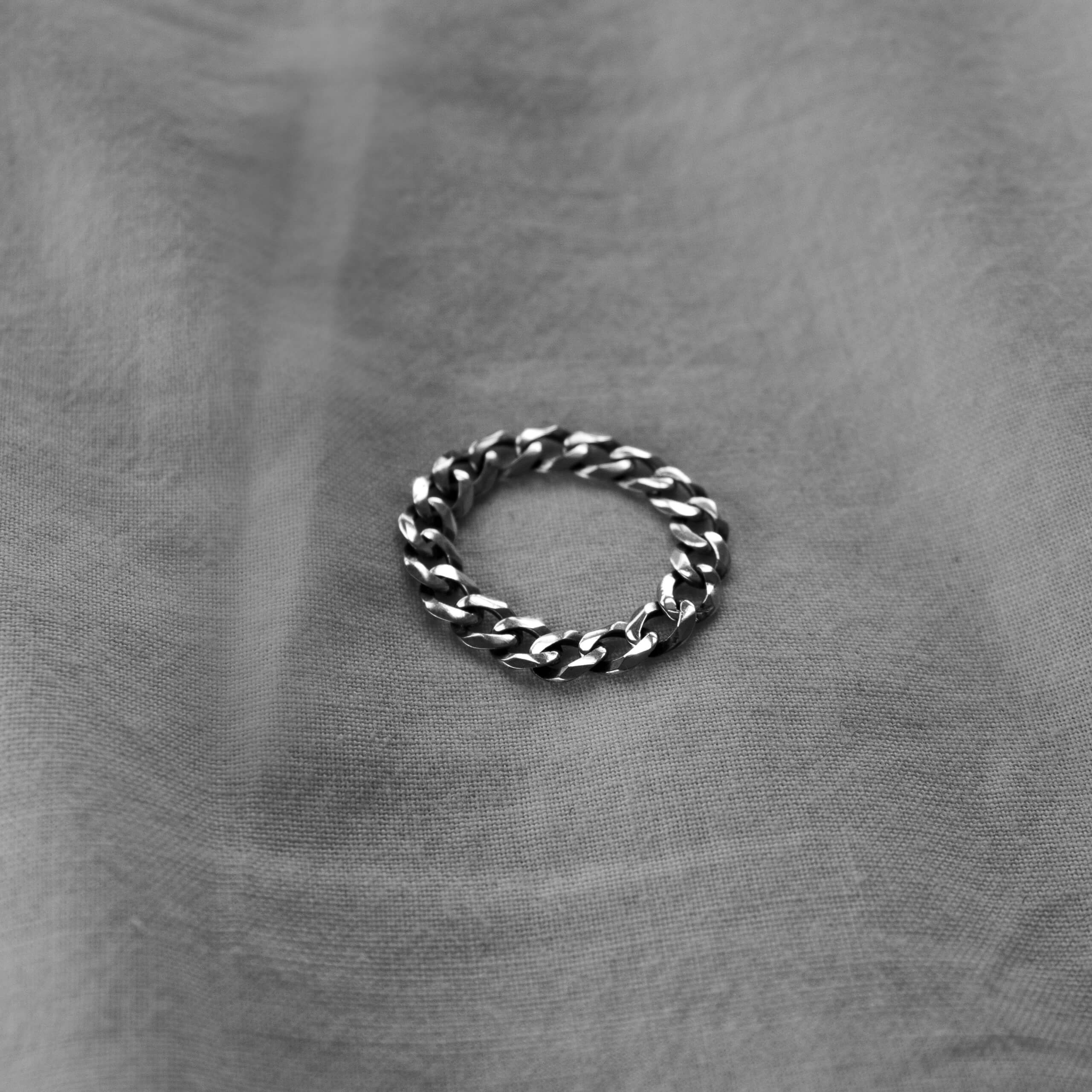 Pierścionek łańcuch ze srebra na jasnym materiale, zdjęcie czarno-białe.
