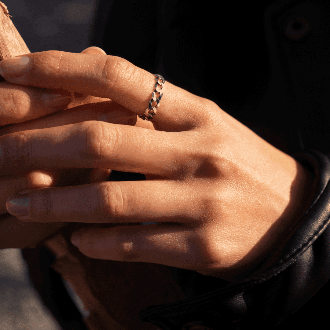 Modelka prezentuje na dłoni srebrny pierścionek łańcuch trzymając suchy liść.