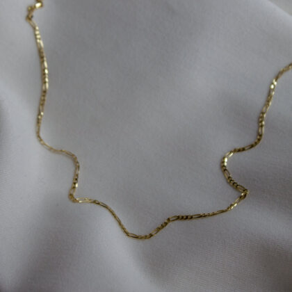 Figaro weave gold chain on light-colored fabric.