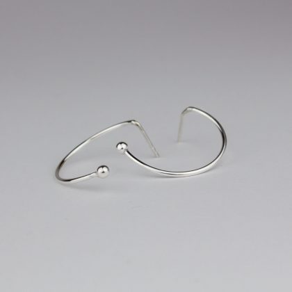 Silver semicircle earrings are on white table.